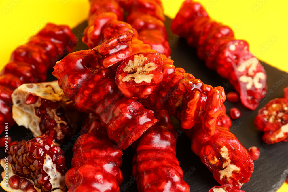 Slate board with tasty churchkhela and pomegranate on yellow background, closeup