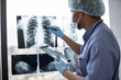 © sofiko14 - Focus on chest X-ray examination studied by multiracial healthcare practitioner in protective garment using tablet with stylus pen. Male radiologist identifying mass in left lung using technologies.