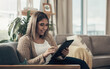 © N F/peopleimages.com - Turning her happy space into a social space. a young woman using a digital tablet on the sofa at home.