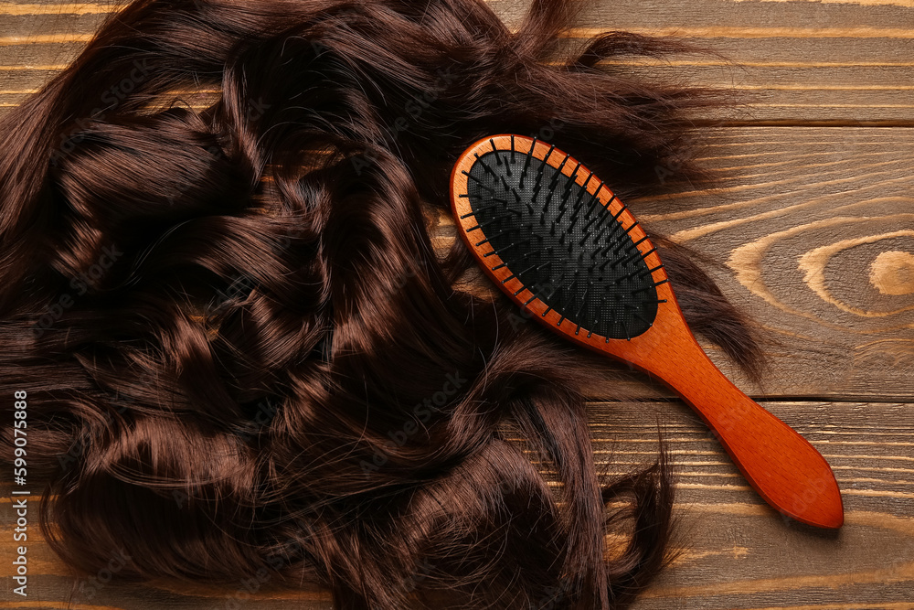 Curled brown hair with brush on wooden background