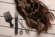 Curled brown hair with scissors and brushes on grey wooden background