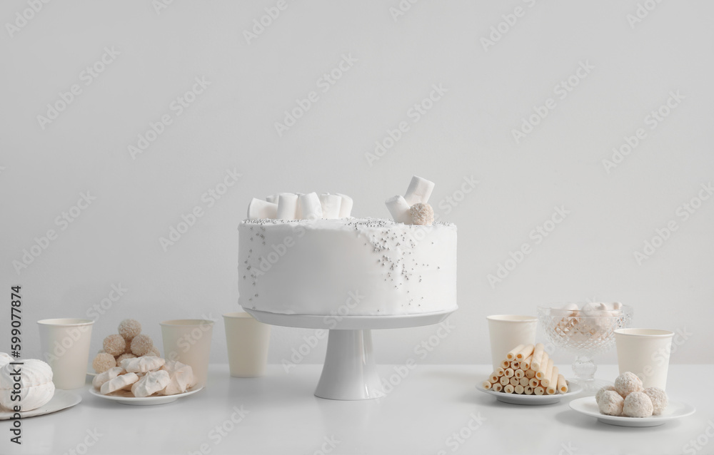 Birthday cake and sweets on white table near wall