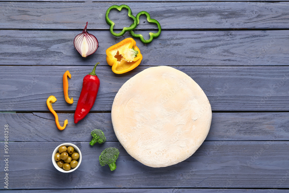 Raw dough and ingredients for preparing vegetable pie on blue wooden background