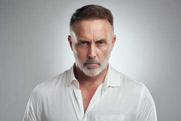 I dont find that funny at all. Studio portrait of a mature man looking angry against a grey background.