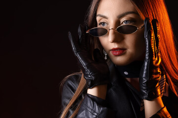 Sticker - Beautiful young woman in leather gloves and jacket on dark background