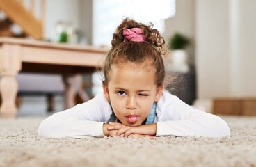 Wall Mural - Kids love being silly. Portrait of an adorable little girl making a face while lying on the floor at home.