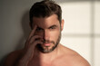 Close up beauty portrait of half naked satisfied young man after facial cream. Attractive brunet guy touching skin. Men model face with beard and modern haircut.