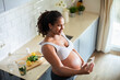 Young pregnant latina woman using a smart phone and having a video call while in the kitchen of a house