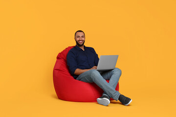 Poster - Smiling young man working with laptop on beanbag chair against yellow background