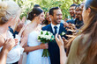 © Nina L/peopleimages.com - Happy bride and groom standing together while greeting guests after their wedding ceremony. Newlyweds smiling while friends and family congratulate them on their marriage