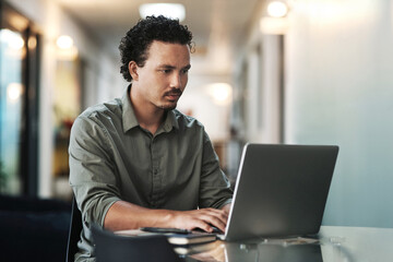 One more email and then Im done. a handsome young businessman sitting alone in the office and using his laptop.