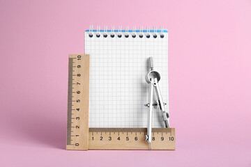 Rulers, notebook and compass on pink background