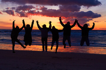 Beach, sunset and silhouette of jumping friends in nature, freedom and celebrating travel outdoor. Shadow, jump and group of people at the ocean and sunrise for adventure, celebration or sea vacation