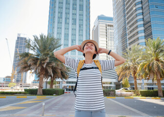 travel to the United Arab Emirates, Happy young asian female traveler with backpack and hat in big city of Abu Dhabi. Vacation and tourist destination concept.