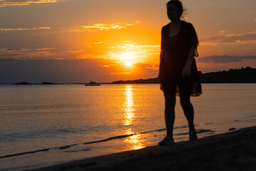 Wall Mural - Brunette woman looks at the sunset on the beach