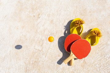 Two ping pong racket and two yellow flip flop just as a ball bounces on the ground.