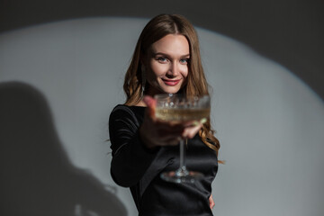 Happy beautiful chic woman with a smile in a fashionable elegant black dress holding a vintage glass of champagne at a party. Pretty lady celebration