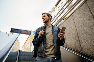 Man using smartphone while going down to subway on escalator