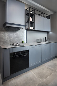 Blue grey contemporary kitchen linearlayout with hood two burners gas cooker hob oven and built in dishwasher machine and square black sink and tap compact high pressure laminate HPL countertop.