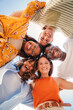 © Jose Calsina - Vertical. Low angle view of a group of five multiracial teenagers smiling and looking down at camera outdoors. Young student people of diverse ethnic cultures embracing while standing in a circle