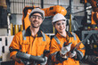 happy young engineer working together service team with robot welding in automation factory. Man and woman smiling worker in safety suit staff worker in automated technology manufacturing industry.