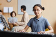 © Seventyfour - Portrait of schoolgirl looking at camera while learning to play piano in music class
