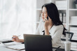 © Kritdanai - Cheerful business lady working on laptop in office, Asian happy beautiful businesswoman in formal suit work in workplace. Attractive female employee office worker smile.