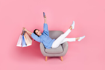 Poster - Full length photo of pretty excited person sit chair hold boutique bags telephone isolated on pink color background