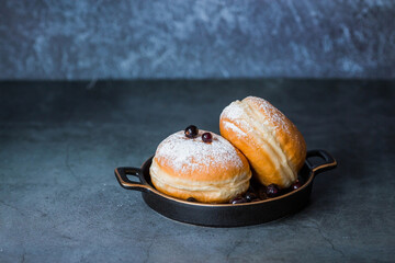 Delicious dessert. A doughnut with berry filling, fresh currant berries and powdered sugar on a stylish ceramic plate on a dark background. Sweets.