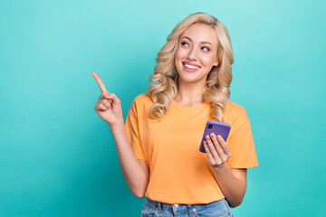 Poster - Portrait of optimistic person wear stylish t-shirt hold smartphone look indicating empty space isolated on turquoise color background