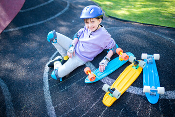 Wall Mural - a child in a purple helmet sits next to multi-colored plastic city cruisers, skateboards.