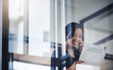 Canvas Print - All looks positive from my side. a young businesswoman talking on a cellphone while going through paperwork in an office.