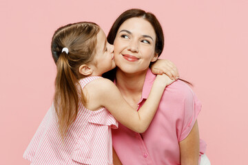 Wall Mural - Happy fun adorable lovely woman wearing casual clothes with child kid girl 6-7 years old. Daughter kissing mother cheek, look aside isolated on plain pastel pink background. Family parent day concept.