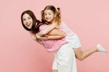 Wall Mural - Sideways woman wear casual clothes with child kid girl 6-7 years old. Mother, give piggyback ride to joyful daughter sitting on back isolated on plain pastel pink background Family parent day concept