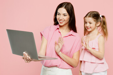 Wall Mural - Happy IT woman wear casual clothes with child kid girl 6-7 years old. Mother daughter work hold use laptop pc computer waving hand isolated on plain pastel pink background. Family parent day concept.