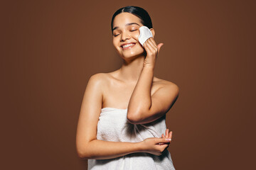 Wall Mural - Facial exfoliation: Young woman cleans her face with a facial sponge