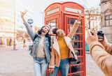 Fototapeta Londyn - two friend, girlfriend and women using a mobile phone, camera and taking selfie against a red phonebox in the city of England.Travel Lifestyle concept