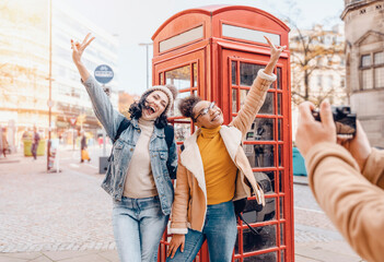 two friend, girlfriend and women using a mobile phone, camera and taking selfie against a red phonebox in the city of England.Travel Lifestyle concept