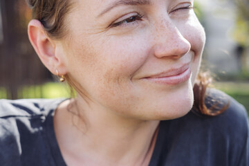 Close up portrait of a young  relaxed woman smiling and looking aside. Outdoors, green park 