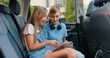 © serg - Attractive joyful blond 10-12-year-old kids sitting on car's backseat and enjoying games on tablet gadget,entertainment during car trip