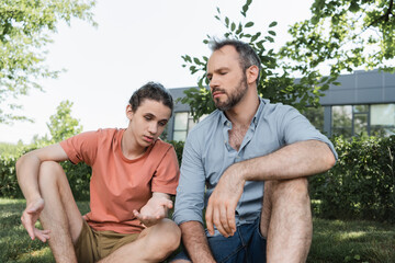 Wall Mural - bearded father sitting next to teenage son while talking in green park.