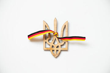 Wall Mural - Wooden trident of Ukraine and the ribbon of the flag of Germany tied to a trident on a white background, friendship and union