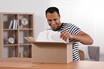 Wall Mural - Happy young man opening parcel at table indoors. Internet shopping