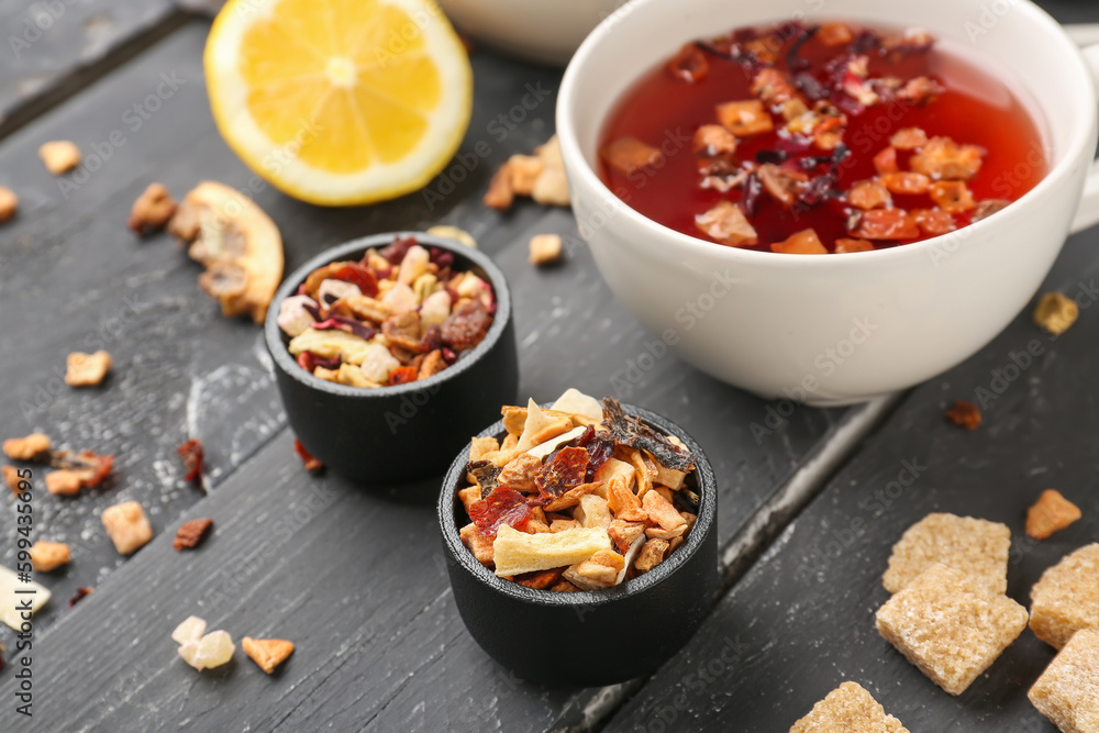 Bowls with dried fruit tea on black wooden table, closeup