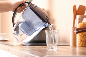 Wall Mural - Woman pouring water from modern filter jug into glass on kitchen counter