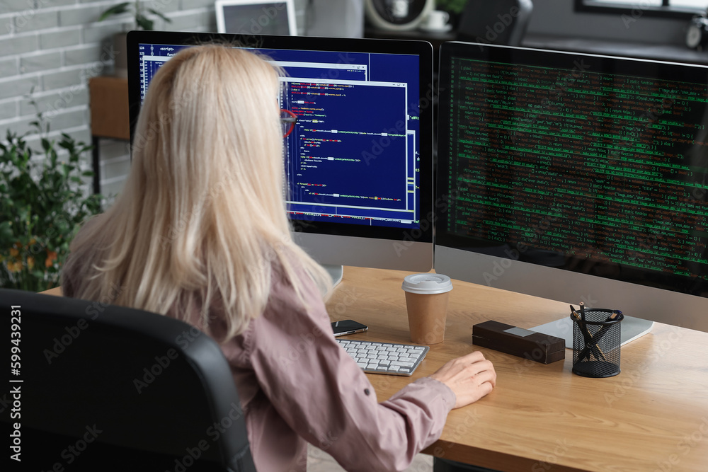 Mature female programmer working with computer at table in office