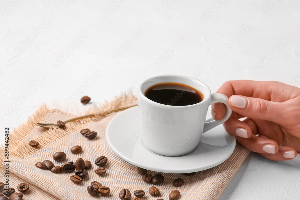 Female hand with cup of coffee and beans on light background
