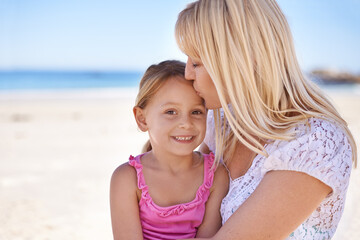 Wall Mural - Mommys little girl. A loving mother giving her daughter a kiss on the forehead while at the beach.