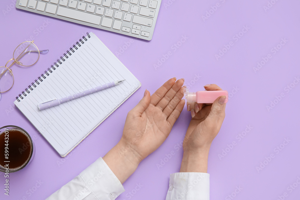 Woman applying hand sanitizer at lilac table in office