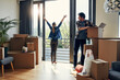© GR/peopleimages.com - Hello there neighbors. a cheerful middle aged woman stretching her arms out on her balcony while her husband looks at her and packs out boxes on moving day.